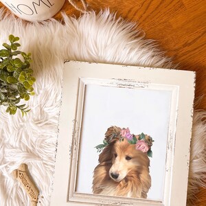 May include: A framed print of a dog wearing a flower crown. The dog is a brown and white Collie with a white background. The frame is white with a distressed look.