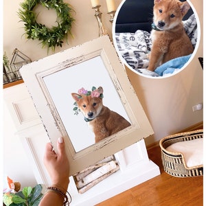 May include: A framed print of a Shiba Inu puppy wearing a flower crown. The puppy is sitting on a white background and looking at the camera. The frame is white with a distressed finish.