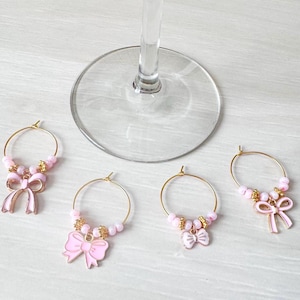May include: Four gold-toned wine glass charms with pink bows and beads.