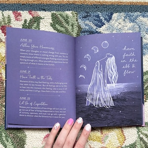 May include: An open book with a purple cover, featuring text and illustrations. The left page has text about June 20, 21, and 22. The right page has a drawing of a person with long hair, the moon, and the text "have faith in the ebb & flow."