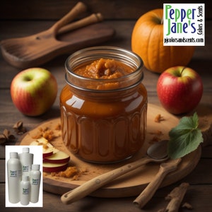 May include: A jar of orange-brown preserves sits on a wooden cutting board, surrounded by a red apple, a green apple, and a small pumpkin. Wooden spoons and cinnamon sticks are also present. The image includes the text "Pepper Jane's Colors & Scents".