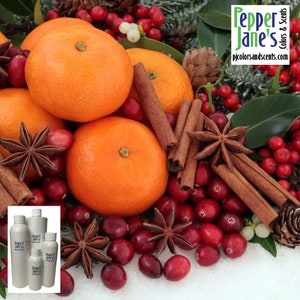 May include: A festive arrangement featuring bright orange tangerines, cinnamon sticks, star anise, and red cranberries. The image includes a small cluster of white bottles with the text "Pepper Jane's Colors & Scents" and the website address.