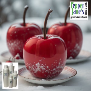May include: Three glossy red apple-shaped ornaments with brown stems, dusted with white accents, sit on small plates. The background is blurred, suggesting a snowy scene. The image also includes several white bottles with the text "Pepper Jane's Colors & Scents".