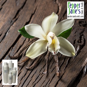 May include: A white orchid flower with green leaves and vanilla beans on a brown wooden surface. The image also includes a logo for Pepper Jane's Colors & Scents with the website address pjcolorsandscents.com.