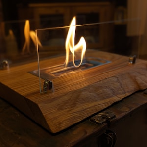 Peut inclure: Un foyer de table avec un enclos en verre et une base en bois. Le foyer est allumé et les flammes sont visibles à travers le verre.