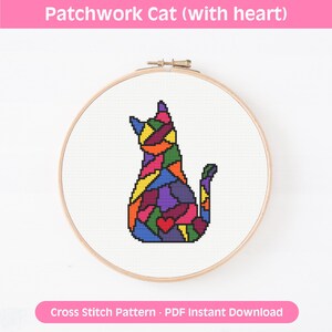 May include: A cross stitch pattern in a wooden embroidery hoop featuring a cat silhouette filled with a multicolored patchwork design of geometric shapes and a small red heart on the lower body, set against a plain white fabric background.