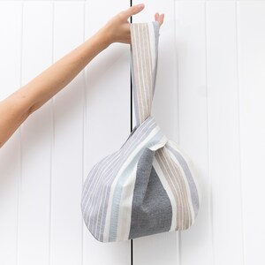 Puede incluir: Una bolsa de tela de mano con rayas grises y beige y asas anudadas.