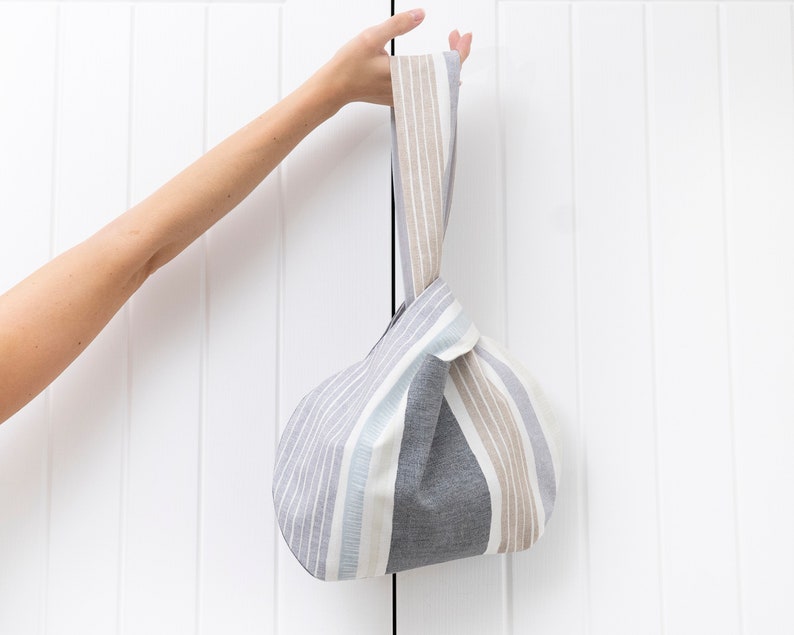 Puede incluir: Una bolsa de tela de mano con rayas grises y beige y asas anudadas.