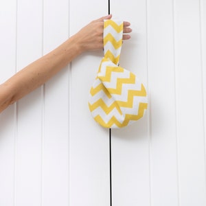 Puede incluir: Una bolsa de tela amarilla y blanca con un patr&oacute;n de zigzag. La bolsa est&aacute; atada con un nudo en la parte superior y tiene un asa.