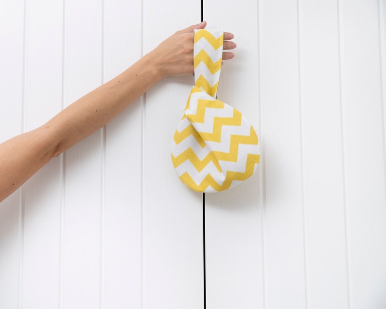 Puede incluir: Una bolsa de tela amarilla y blanca con un patr&oacute;n de zigzag. La bolsa est&aacute; atada con un nudo en la parte superior y tiene un asa.