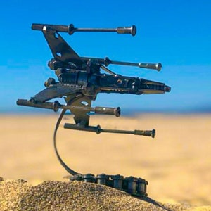 May include: A metal sculpture of a spaceship made from recycled materials. The spaceship is black and has a long, thin body with two wings. It is sitting on a stand made of metal chain.