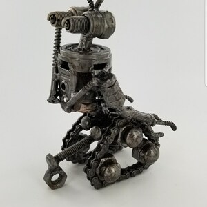 Puede incluir: Una peque&ntilde;a escultura de robot hecha de piezas de metal recicladas. La escultura est&aacute; hecha de tuercas, tornillos, tornillos y otras piezas de metal. El robot tiene un sistema de orugas de cadena y una cabeza hecha de buj&iacute;as.