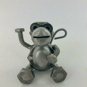 May include: A small, silver metal monkey sculpture made from nuts and bolts. The monkey is sitting with its arms raised and its tail curled behind it.