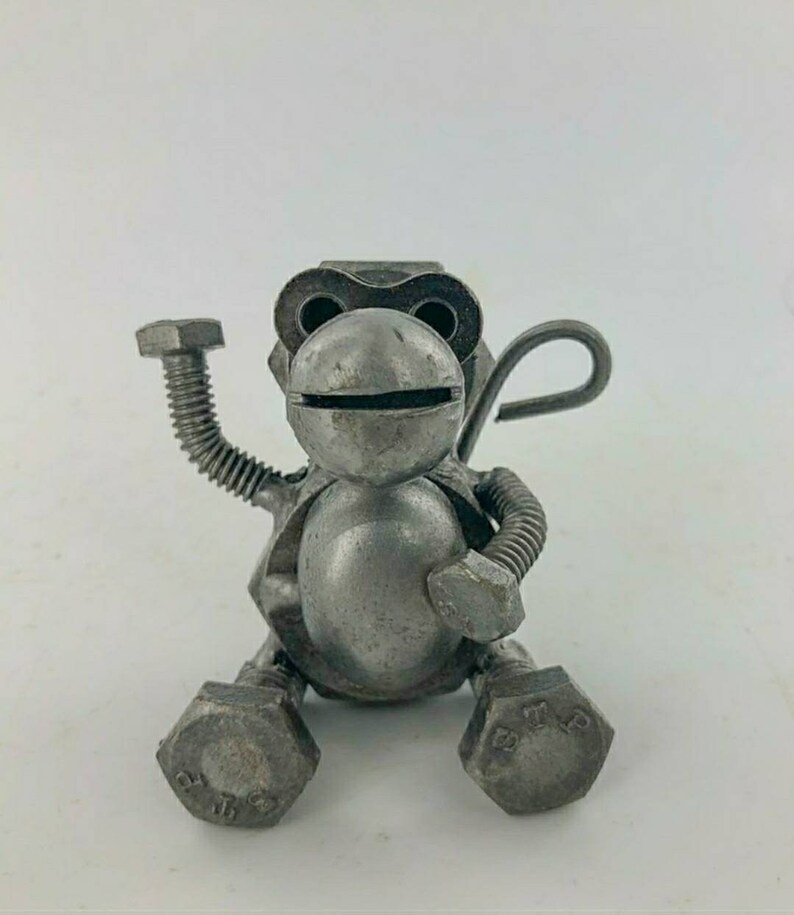 May include: A small, silver metal monkey sculpture made from nuts and bolts. The monkey is sitting with its arms raised and its tail curled behind it.