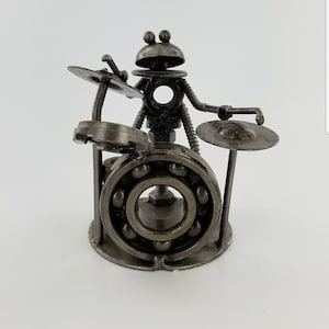 May include: A metal sculpture of a robot playing the drums. The robot is made of nuts, bolts, and other metal parts. The drums are made of a large bearing and smaller metal discs.