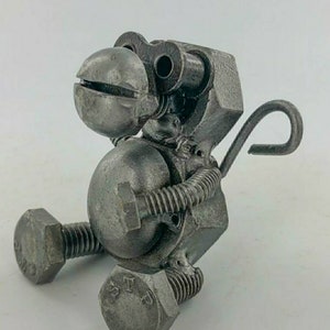 May include: A small, grey metal monkey sculpture made from nuts, bolts, and other hardware. The monkey is sitting with its legs bent and its tail curled up behind it.