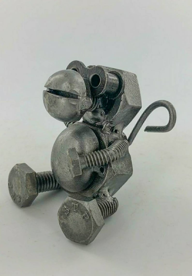 May include: A small, grey metal monkey sculpture made from nuts, bolts, and other hardware. The monkey is sitting with its legs bent and its tail curled up behind it.