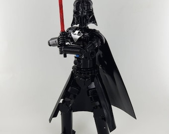 May include: A black metal sculpture of Darth Vader from Star Wars. The sculpture is holding a red lightsaber and is wearing a black cape.