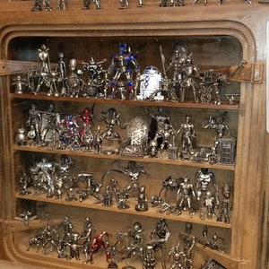 May include: A wooden shelf unit with multiple shelves filled with metal figurines of popular characters. The figurines are made of recycled metal and are painted in various colours, including silver, black, red, and blue.