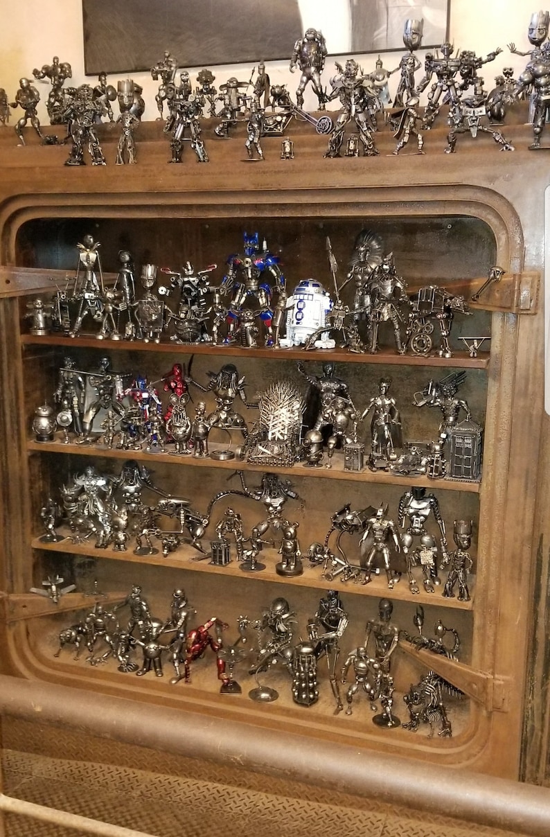 May include: A wooden shelf unit with multiple shelves filled with metal figurines of popular characters. The figurines are made of recycled metal and are painted in various colours, including silver, black, red, and blue.