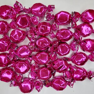 May include: A collection of sweets, each wrapped in bright pink, shiny foil. The sweets are round with an octagonal shape, and the foil has a polka dot pattern. The foil is twisted at the ends.