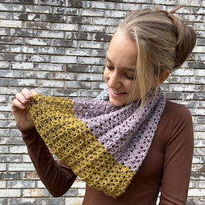 May include: A crocheted scarf with a two-tone color pattern. The scarf is a light purple color on one side and a mustard yellow color on the other side.