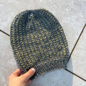 May include: A gray and yellow knitted beanie hat with a ribbed texture.