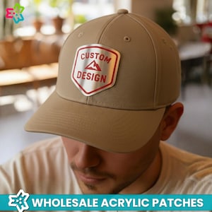 May include: Tan baseball cap with a silver and red "CUSTOM DESIGN" patch. The patch features a mountain graphic. The cap has a curved brim and a button on top. The text "WHOLESALE ACRYLIC PATCHES" is at the bottom.