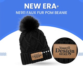 May include: Black knit beanie with a faux fur pom and a leather patch that says "Your Design Here." The beanie is a New Era NE911 style. The image also shows a close-up of the leather patch.