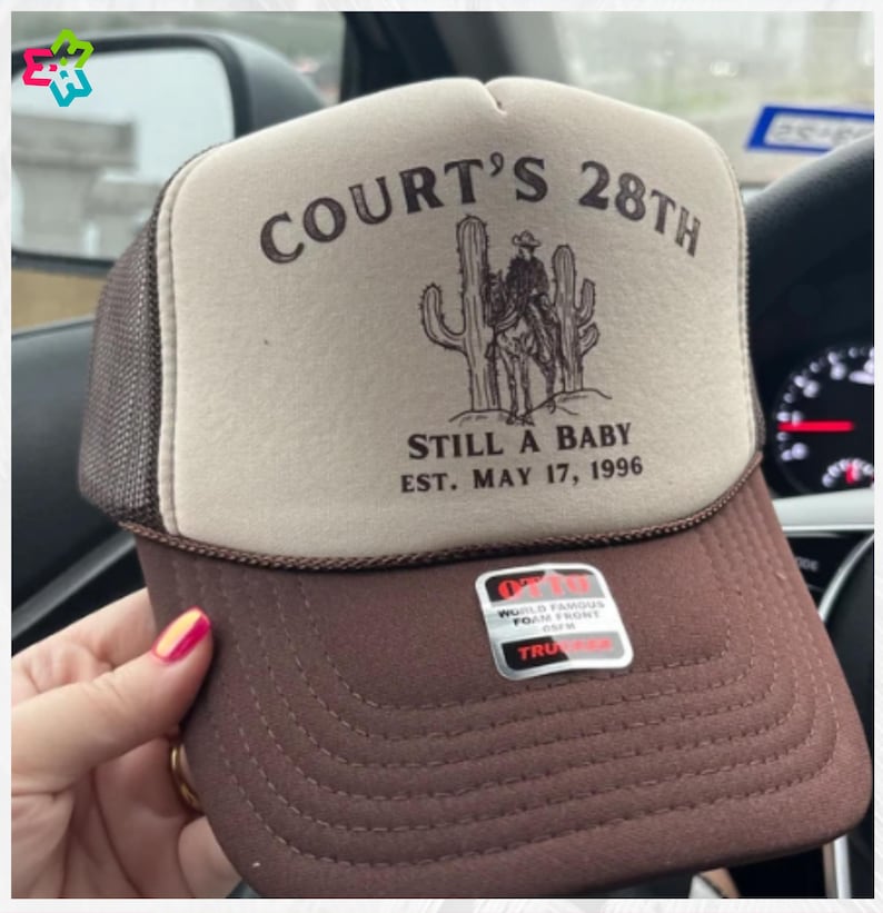 Puede incluir: Gorra de camionero marr&oacute;n y beige con el texto "COURT'S 28TH" sobre un dibujo de un vaquero y cactus. La gorra tambi&eacute;n muestra "STILL A BABY EST. MAY 17, 1996".