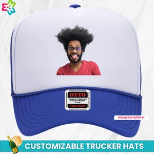 May include: A blue, white, and royal blue trucker hat with a custom photo of a person with a beard and glasses. The hat has a mesh back and a foam front. The text "OTTO WORLD FAMOUS FOAM FRONT OSFM TRUCKER" is printed on the front of the hat.