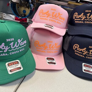Op de afbeelding: Een collectie van vijf truckerpetten in groen, roze en marineblauw. Elke pet is voorzien van de geborduurde tekst 2025 Party Wave Nosara, Costa Rica. De petten hebben een mesh achterkant, een schuimrubberen voorkant en een Otto-sticker op de klep.