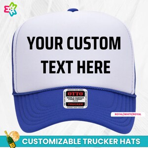 May include: A white and royal blue trucker hat with a black "YOUR CUSTOM TEXT HERE" message on the front. The hat has a black and red label that says "OTTO WORLD FAMOUS FOAM FRONT OSFM TRUCKER".