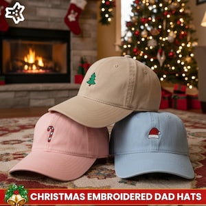 May include: Three baseball caps in tan, pink, and light blue, each embroidered with a Christmas design: a green tree, a candy cane, and a Santa hat. The caps are displayed in front of a Christmas tree and fireplace.