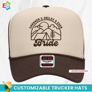 K&ouml;nnte beinhalten: Ein beige-brauner Trucker-Hut mit einer braunen Umrandung einer Bergszene und einem Zelt. Der Text "GARDNER & HAILEY 4 EVER" befindet sich &uuml;ber der Szene und das Wort "Bride" unter der Szene. Der Hut hat ein braunes Netzr&uuml;cken und einen braunen Druckknopfverschluss.