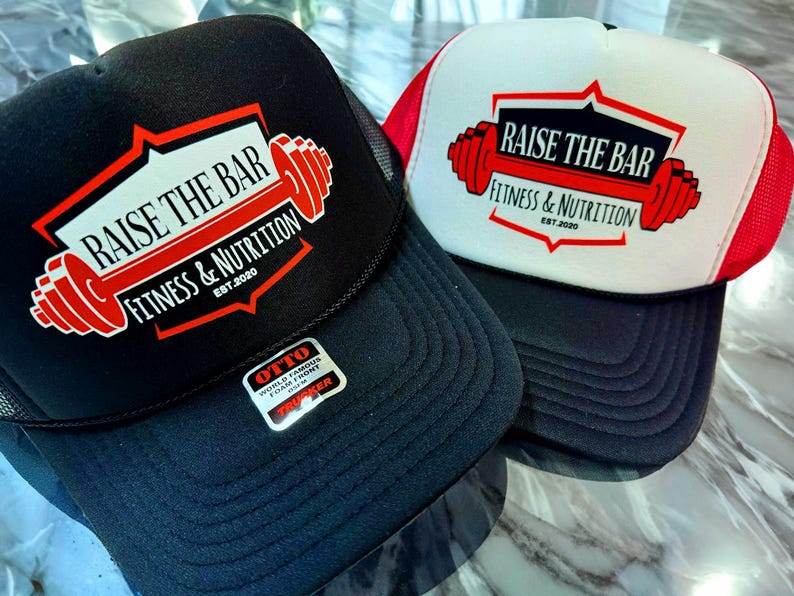 DTF printed OTTO® foam trucker hats with "Raise the Bar Fitness & Nutrition" design. Black and white/red colorways with bold barbell logo, perfect for gym merch or personal trainers. Durable foam front, breathable mesh back.