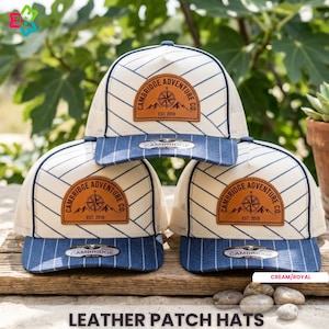 May include: Cream and royal blue trucker hats with a leather patch featuring the text "CAMBRIDGE ADVENTURE CO. EST. 2019." The hats have a striped design and a curved brim. The image also includes the text "LEATHER PATCH HATS."