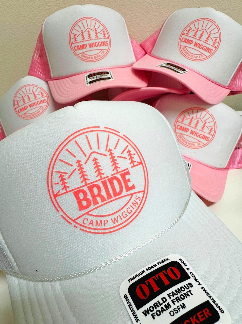 Custom pink and white OTTO foam trucker hats featuring a “Camp Wiggins” design in light red. The bride’s hat is customized with bold “BRIDE” text at the center, while the bridesmaid hats display only “Camp Wiggins.” Perfect for bachelorette parties or group camping trips.