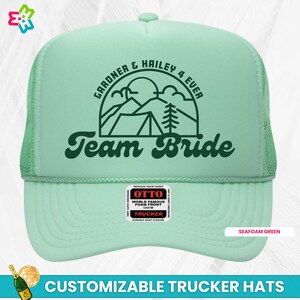 K&ouml;nnte beinhalten: Trucker-Kappe in Seefraben-Gr&uuml;n mit einer gr&uuml;nen Bergszene und dem Text "GARDNER & HAILEY 4 EVER Team Bride". Die Kappe hat ein schwarzes Netzr&uuml;cken und einen schwarzen Druckknopfverschluss.