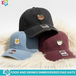 May include: Three embroidered dad hats in black, light blue, and burgundy. The black hat features a ramen bowl, the light blue hat has a fried egg, and the burgundy hat displays a coffee cup. The hats are on a fluffy white surface. Text at the bottom reads "FOOD AND DRINKS EMBROIDERED DAD HATS."