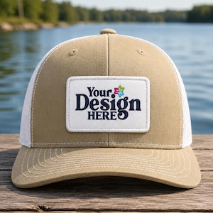 May include: A tan baseball cap with a white mesh back and a white rectangular patch on the front. The patch features the dark blue text "Your Design HERE" with a small, colorful, multi-petaled flower icon positioned above the word Design.