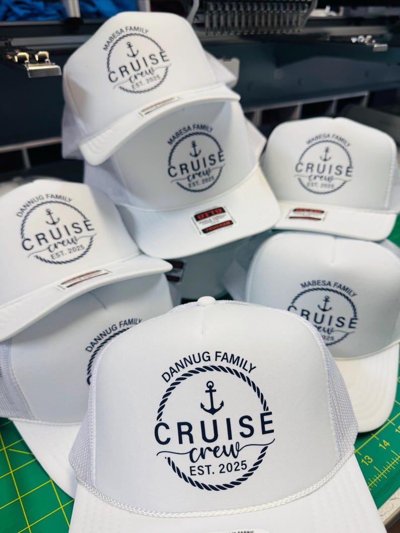 May include: A collection of white trucker hats with a mesh back and a curved brim. Each hat features a circular design with an anchor, the words "CRUISE CREW", and the year "EST. 2025" or "EST. 2021". The hats are branded with "MABESA FAMILY" and "DANNUG FAMILY".