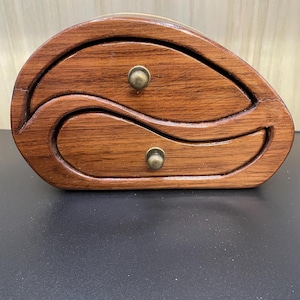May include: A wooden box with two drawers, each with a brass knob. The box is shaped like a wave and has a dark brown stain.