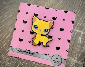 May include: Yellow cat enamel pin with blue eyes on a pink background with black paw prints and the text "@ACTION_PINS".