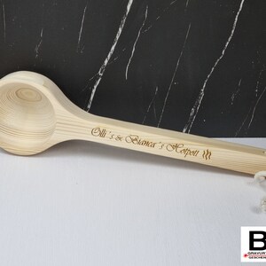 Könnte beinhalten: Eine hölzerne Schöpfkelle mit einem langen Stiel und einer abgerundeten Schüssel. Der Stiel ist mit dem Text "Olli's & Bianca's Hotpot!!!" graviert.