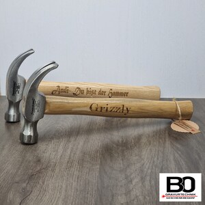 Könnte beinhalten: Zwei Hämmer mit Holzstielen und silbernen Köpfen. Die Stiele sind mit dem Text "Andi - Du bist der Hammer" und "Grizzly" graviert.