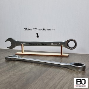 Peut inclure: Une clé à molette argentée avec une inscription noire qui dit "Bianca & Oliver" sur un support en bois. La clé est de 19 mm et possède un mécanisme à cliquet.