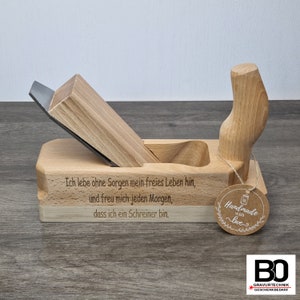 Könnte beinhalten: Ein Holzhobel mit einer Metallklinge. Der Hobel ist mit dem Text "Ich lebe ohne Sorgen mein freies Leben hin, und freu mich jeden Morgen, dass ich ein Schreiner bin." graviert. Ein braunes Etikett mit dem Text "Handmade with love" ist am Hobel befestigt.