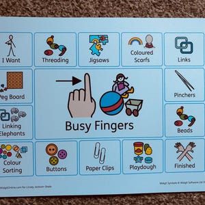 May include: A light blue poster featuring illustrated activity icons such as threading, jigsaws, and colour sorting. The words "Busy Fingers" are in the centre, with the text "I Want", "Peg Board", and "Linking Elephants" also visible. The poster is on a brown surface.