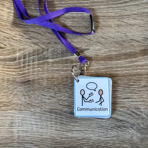 May include: A purple lanyard with a metal clasp, holding a small square card. The card has a blue border and the word "Communication" beneath a stick figure illustration of two people.